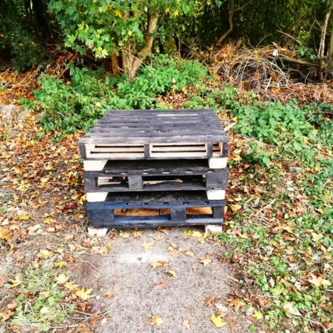 3 wooden pallets stacked at the nd of a pathway in church yard wooded area.